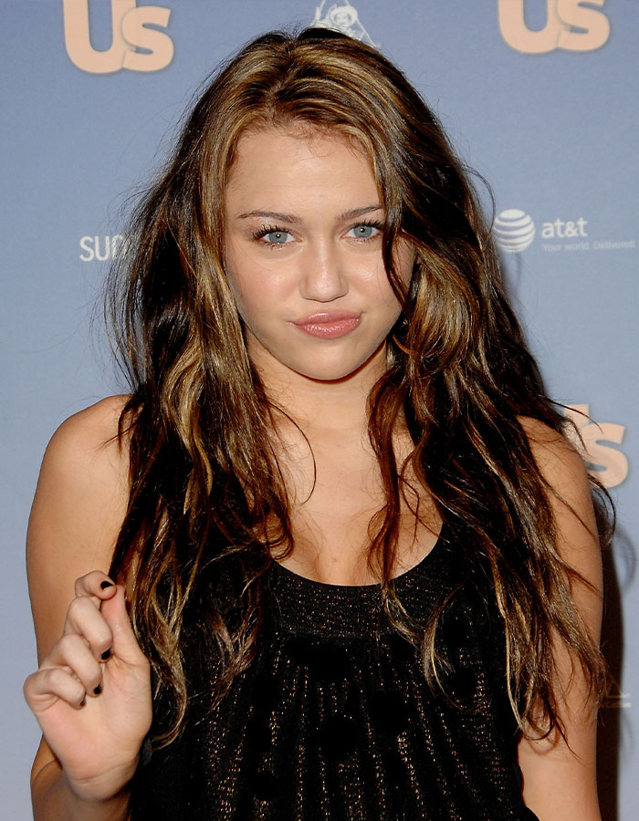 Miley Cyrus posing at an event, with long wavy hair, expressing concern over old interviews about her intimate life.