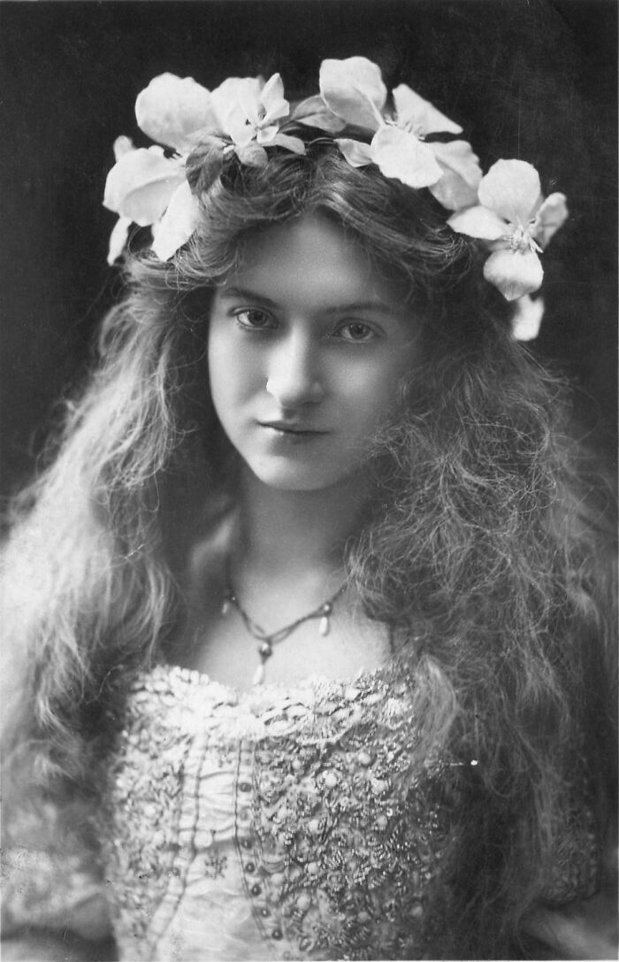 Vintage black and white portrait of a woman with flowers in her hair, representing timeless beauty from a century ago.