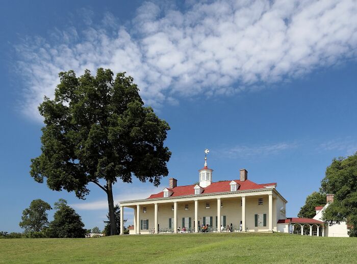 Historic home with large porch and red roof under blue sky, representing America’s architectural heritage.