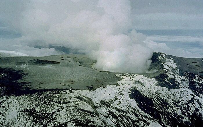 Volcanic eruption with thick smoke rising over rugged terrain, illustrating one of the largest natural disasters.