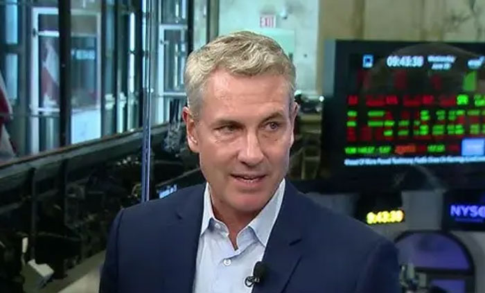 Man in a suit speaking during a broadcast, discussing CEO's past comments and HR chief amid Coldplay scandal.