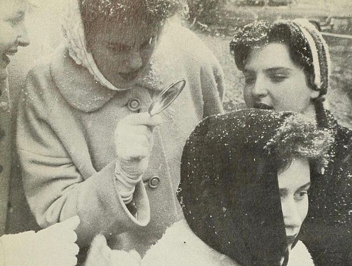 Group of women examining something closely using a magnifying glass in a rare and interesting historical photograph.