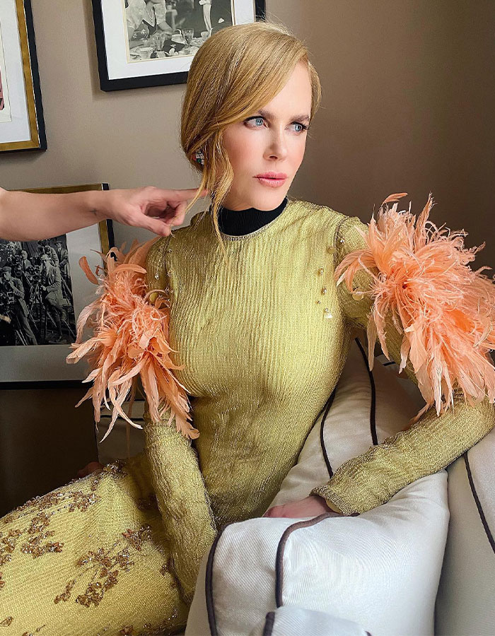 Nicole Kidman styled in gold dress with peach feathered sleeves, showcasing natural curls in a stunning family photo.
