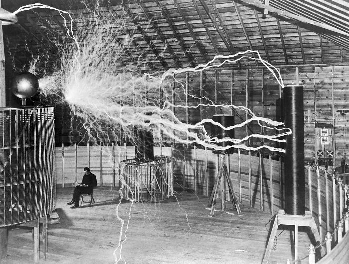 Rare and interesting historical photograph of Nikola Tesla sitting near a large electrical discharge in a lab.