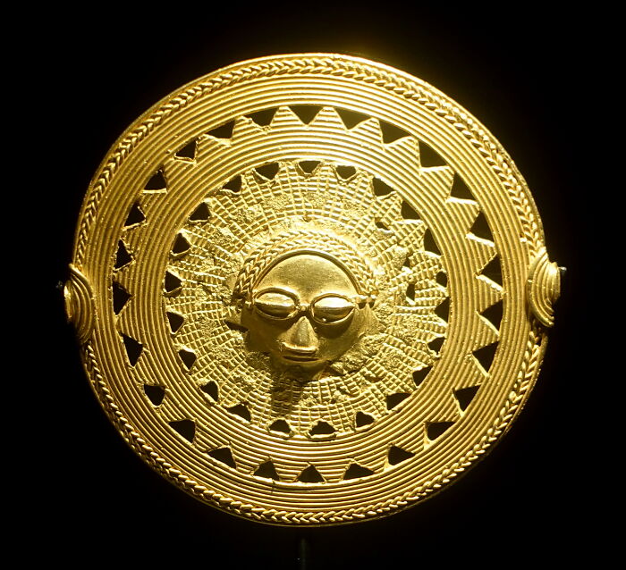 Gold circular foreign artifact with intricate sunburst and face design, part of rare collections held in the British Museum.