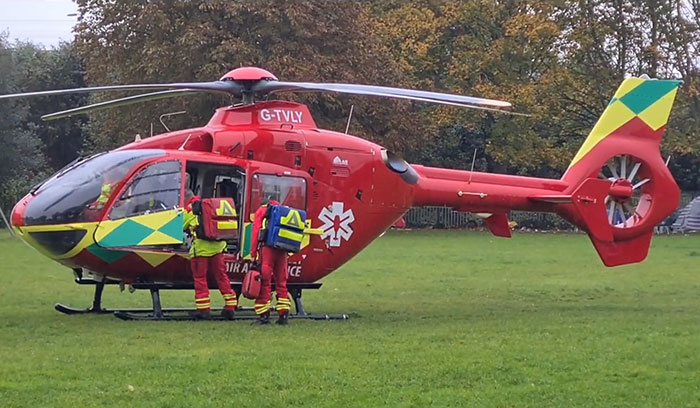 Red air ambulance helicopter on grass with emergency medical crew preparing for a rescue near family home.