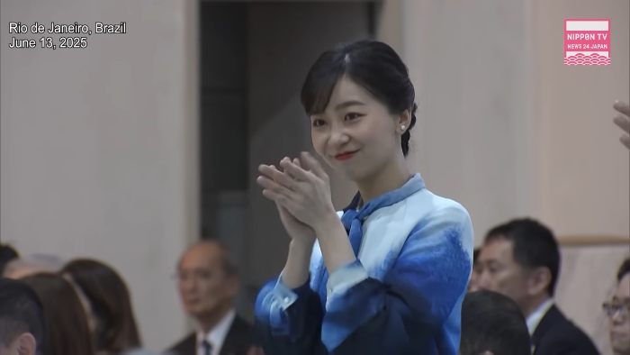 Japanese Princess Kako smiling and applauding at an indoor event, surrounded by seated attendees in formal attire.