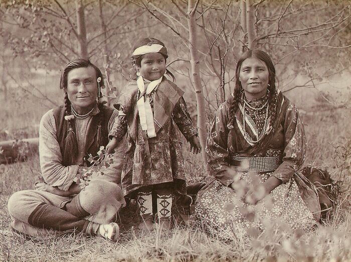 Vintage Native American family portrait outdoors with traditional clothing and natural background in sepia tone.