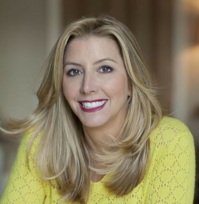 Smiling woman with blonde hair in a yellow sweater, representing the journey from poverty to super wealthy success.