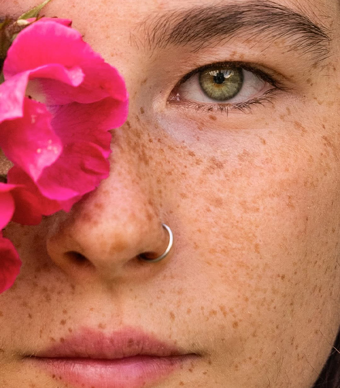 Close-up of a Gen Z woman with freckles, green eyes, and a nose ring, highlighting natural beauty without shaving.
