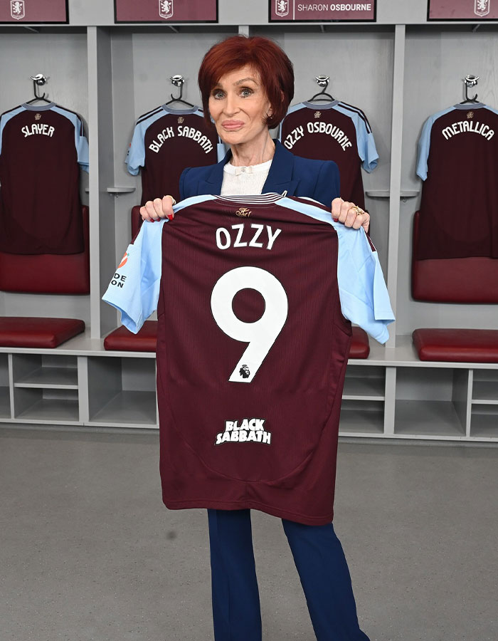 Sharon Osbourne holding a personalized Ozzy football jersey in a locker room with Black Sabbath and Ozzy Osbourne shirts hanging. - 2
