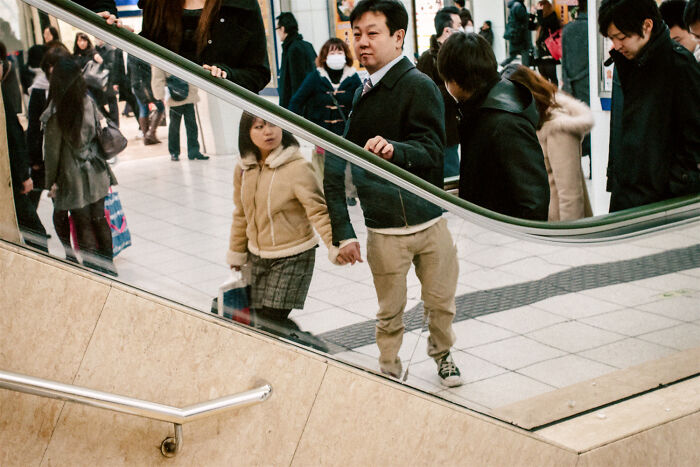 Crowded urban scene reflecting daily life in Japan with people walking and holding hands near a staircase.