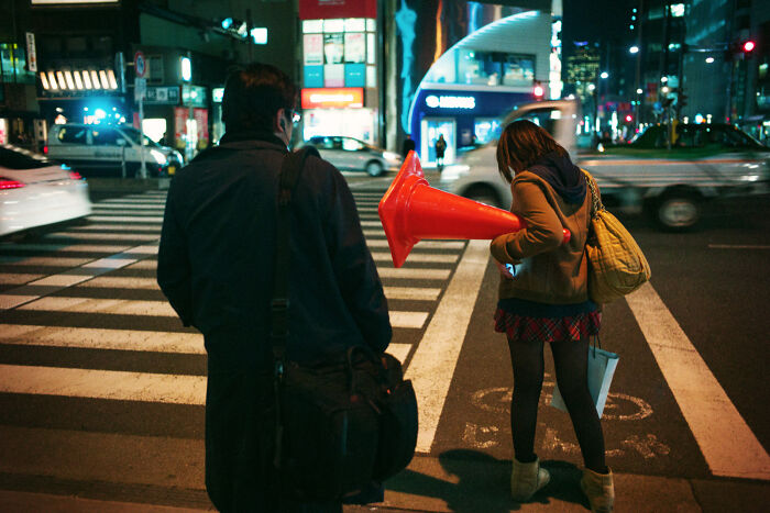 Two people waiting at a crosswalk at night in an urban setting, capturing daily life in Japan by Shin Noguchi.