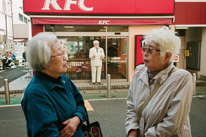 Two elderly women talking outside a KFC in Japan, illustrating daily life and street scenes by Shin Noguchi.