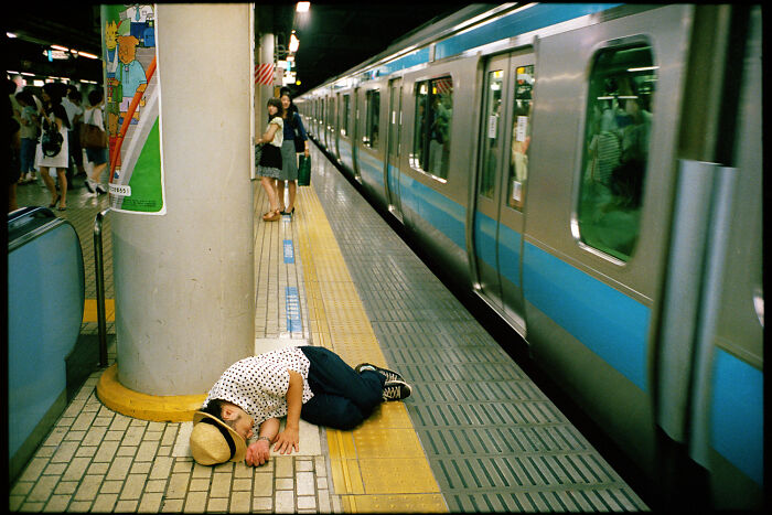 Person sleeping on the floor of a busy train station platform, capturing daily life in Japan through photography.