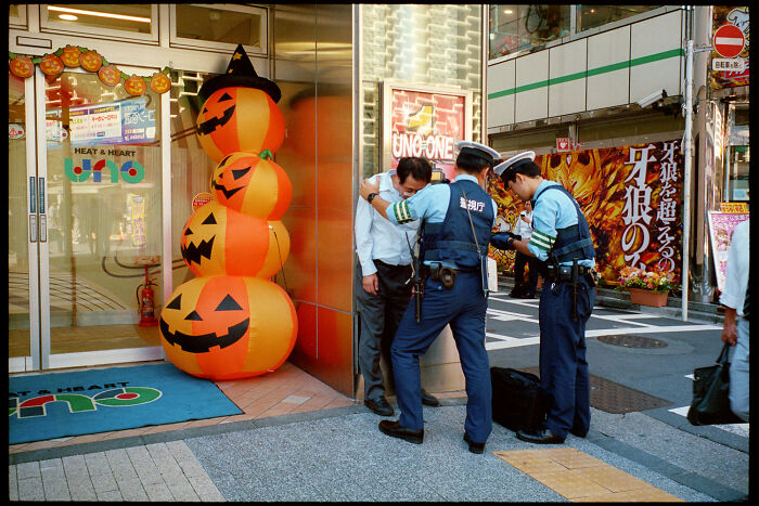Two police officers checking a man on a city street near a Halloween pumpkin decoration in daily life in Japan.