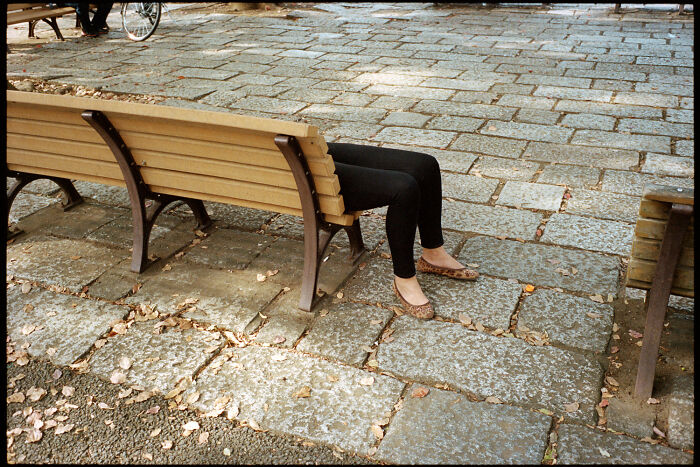 Person in black pants and patterned shoes sitting on a bench in a stone-paved area showing daily life in Japan.