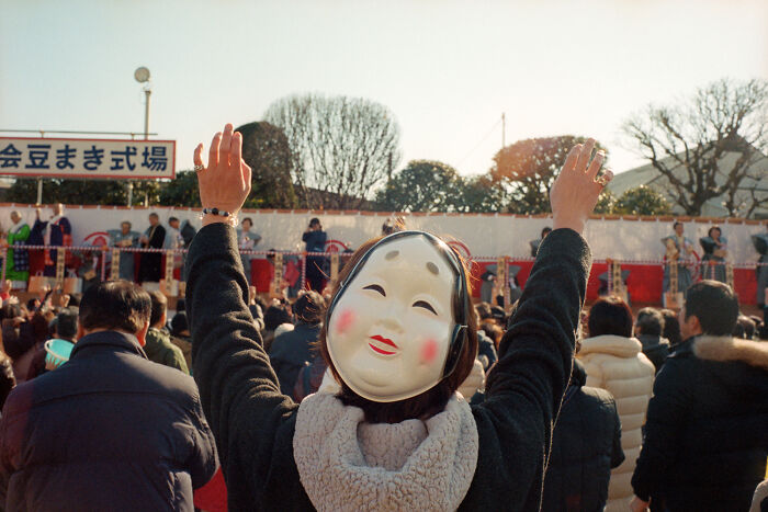 Person wearing traditional mask raising hands in a crowd during a cultural event, showing daily life in Japan.