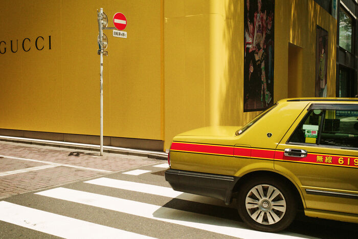 Yellow taxi parked near a Gucci store with a no entry sign in an urban Japan street showing daily life scenes.