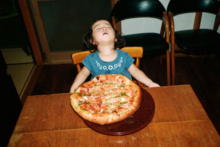 Young child in blue shirt sitting at a table with a large pizza, capturing daily life in Japan by photographer Shin Noguchi.