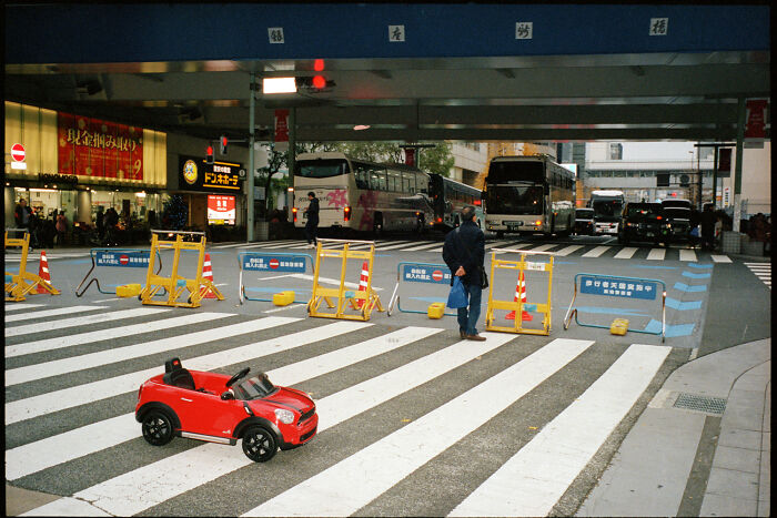 Child's red toy car on a large pedestrian crossing capturing daily life in Japan by photographer Shin Noguchi.