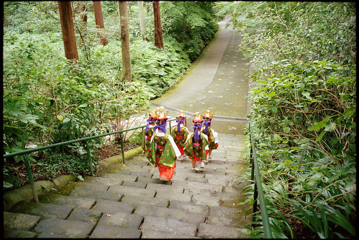 Traditional Japanese dancers in colorful attire descending stone steps surrounded by lush greenery in daily life Japan.
