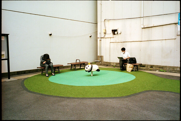 Two people sitting on benches near a panda playground ride, capturing daily life in Japan by Shin Noguchi.