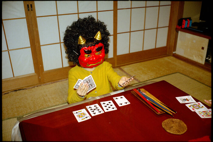 Child wearing a red oni mask playing cards at a low table, capturing daily life in Japan traditions and culture.