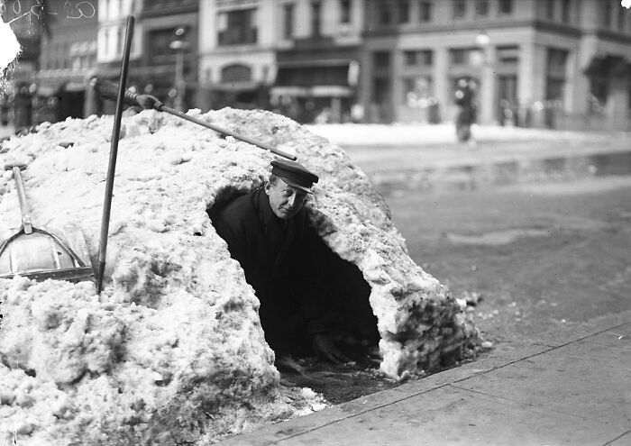 Man emerging from a snow shelter on a city street in a vintage black and white historical photo of Washington, D.C.
