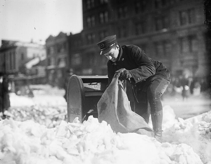 Postal worker collecting mail from a mailbox in snowy Washington, D.C. street, vintage 1920s historical photo.