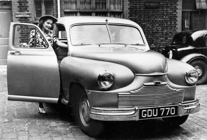 Woman in vintage outfit stepping out of classic car in a rare and interesting historical photograph from the 1940s era.