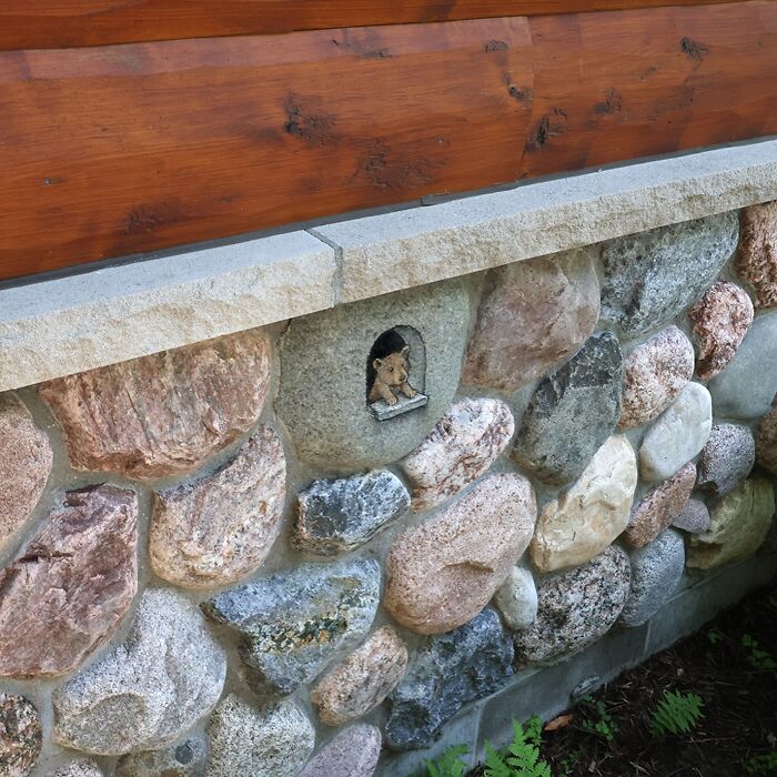 Small chalk drawing of a bear cub peeking through a tiny window in a stone wall, inspired by David Zinn sidewalk art.