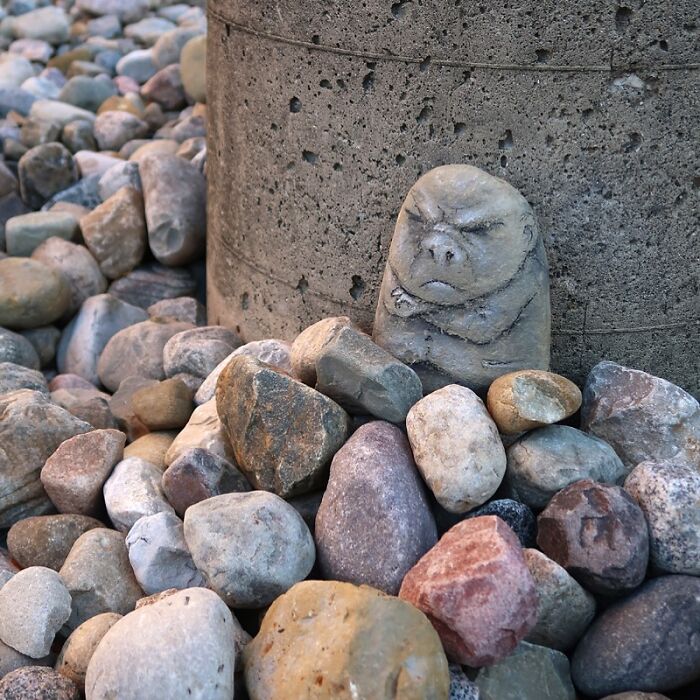 Rock painted with a grumpy face among other stones on a sidewalk, showcasing David Zinn chalk art creativity.