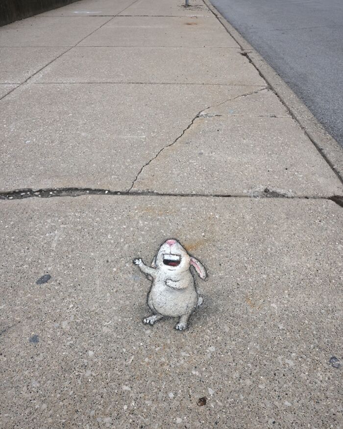 Chalk art of a joyful rabbit drawn on a c*****d sidewalk by David Zinn, turning sidewalks into magical worlds.