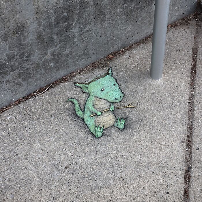 Chalk drawing of a small green dragon on a sidewalk, showcasing David Zinn's magical street art style.