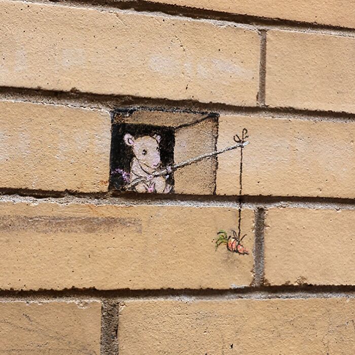 Chalk art by David Zinn showing a mouse fishing for carrots drawn on a brick wall transforming the sidewalk space.
