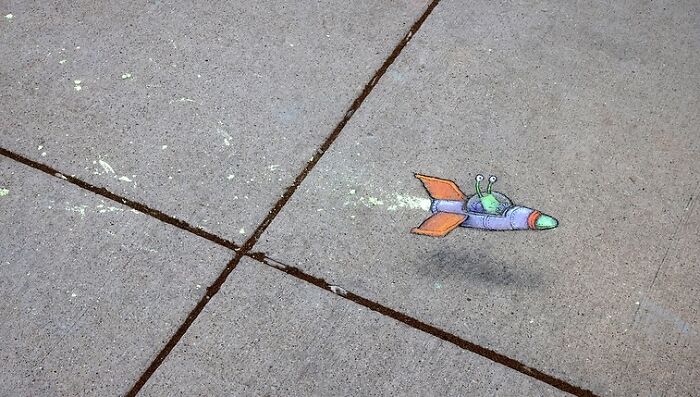 Colorful chalk drawing of a whimsical alien spaceship on a sidewalk by David Zinn, showcasing magical chalk art.
