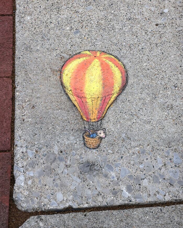 Chalk drawing of a hot air balloon on a sidewalk by David Zinn, creating a magical world on concrete pavement.