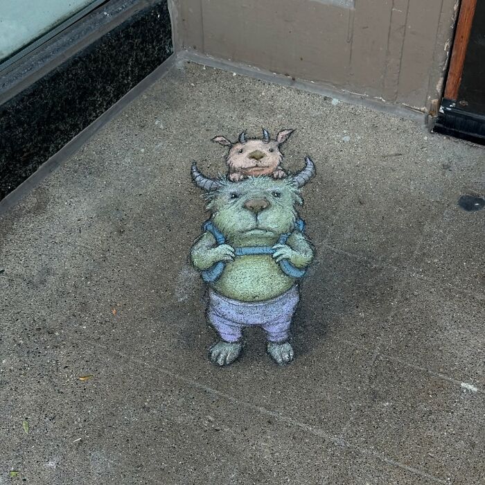 Chalk art by David Zinn showing a whimsical creature with a smaller animal on its head drawn on a sidewalk corner.