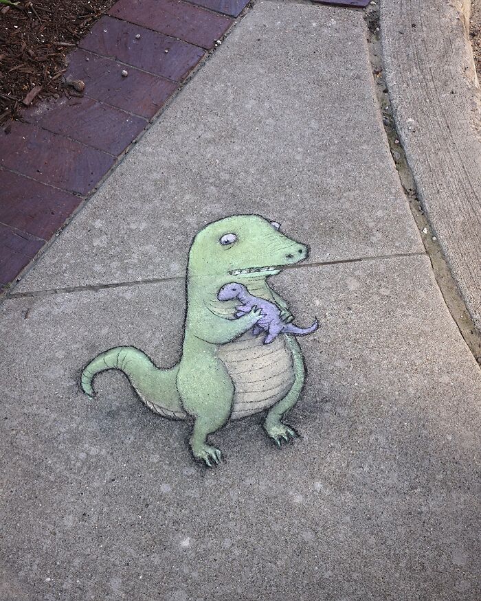 Chalk art by David Zinn on sidewalk showing a green dinosaur holding a smaller purple dinosaur with detailed shading.