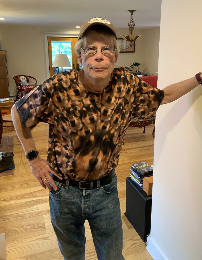 Stephen King standing indoors wearing a dog-patterned shirt and glasses, related to Epstein list conspiracy theories. - 6