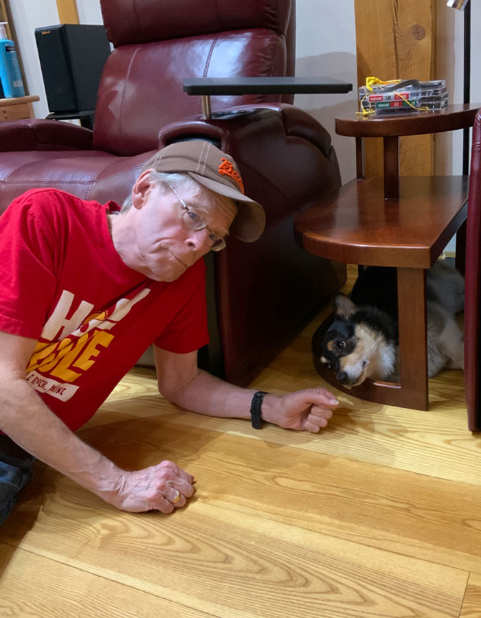 Man in red shirt and cap lying on wooden floor next to a dog under a table, related to Stephen King's Epstein list tweet. - 9