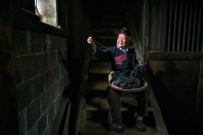 Elderly Asian woman in traditional clothing weaving by hand in dimly lit interior, capturing the soul of Asia.