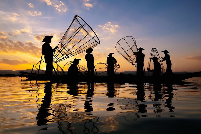 Fishermen silhouetted against a sunset on a lake, capturing the soul of Asia in a stunning cultural scene.