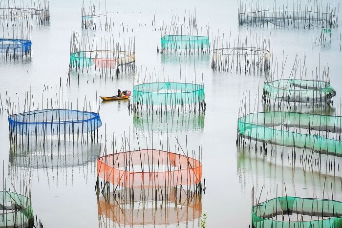 Photographer captures the soul of Asia showing colorful fish traps and a small boat on calm reflective water.