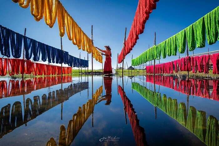 A photographer captures the soul of Asia with vibrant textiles drying over reflective water under a clear blue sky.