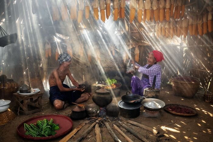 Two people cooking inside a rustic Asian kitchen with sunlight streaming through hanging dried corn, capturing the soul of Asia.
