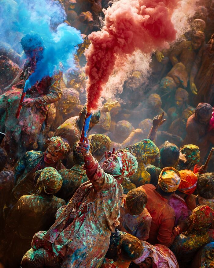 Crowd covered in colorful powders celebrates Holi festival with vibrant smoke flares in a stunning photo capturing the soul of Asia.
