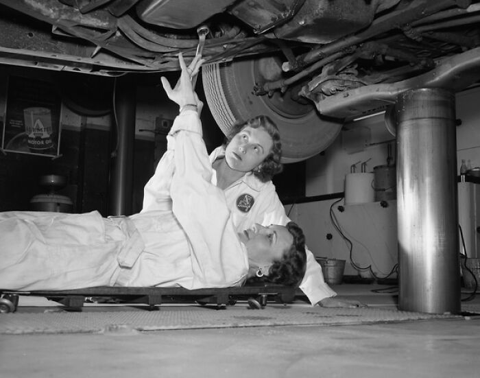 Two women mechanics working under a car in a garage showcasing everyday life in 1950s Florida.