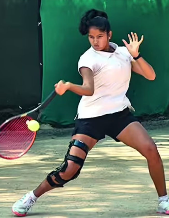 Young female tennis pro wearing knee brace hitting a backhand shot on an outdoor clay court during practice. Young female tennis pro wearing knee brace hitting a backhand shot on an outdoor clay court during practice.